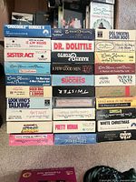 Stacked VHS tapes showing spine titles such as Crocodile Dundee II, Sister Act, Dr. Dolittle, Little House on the Prairie volumes