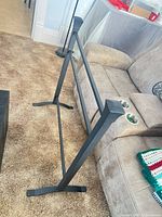 Side view of matte black freestanding metal rack showing square posts, two horizontal bars, and splayed feet