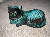 Front/side view of glazed ceramic cat figurine showing black and teal drip glaze finish