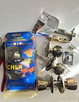 Overall lot showing Schlage deadbolt package, two brass door knob sets, latch components and screws