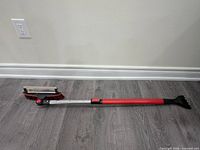 Full view of extendable snow brush showing red handle, aluminum shaft, brush and scraper ends