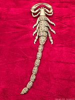 Full view of articulated scorpion brooch on red fabric