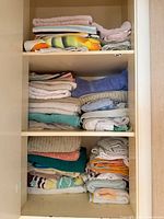Three-shelf cabinet with multiple stacks of assorted towels showing colors, sizes and quantity