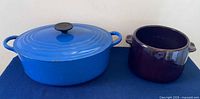 Blue Le Creuset oval Dutch oven beside brown West Bend bean pot