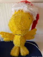 Front view of yellow tinsel Woodstock wearing Santa hat with power cord visible