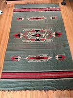 Full view of green Mexican woven rug with geometric patterns and fringe