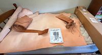 Leather hide, rolled leather strip, laces and pattern booklet laid out on bed