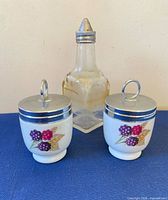 Front view showing two egg coddlers and glass cruet bottle