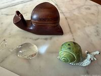 all three items grouped on marble surface: wooden snail box, ceramic snail, glass whale