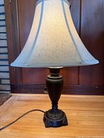 Full view of lamp illuminated showing bronze base and cream bell shade