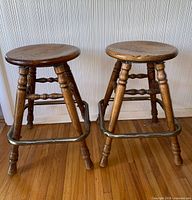 Front view of both oak swivel bar stools showing seats, legs and metal footrests