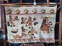 Full view of tapestry hung on framing, showing motifs, colors, hanging rod and overall wear