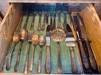 Drawer view showing majority of flatware: spoons, forks, knives, pierced spoon, cake server on green cloth liner