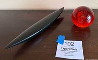 Wooden canoe sculpture and red glass paperweight side by side on surface