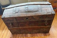 Front and top view of trunk showing curved lid, metal bands, latches, missing lock