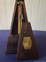 Front view showing metronome with cover removed, brass label, pendulum and scale visible