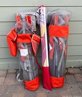 Two red and gray Kijaro chair bags and one umbrella sleeve leaning against wall