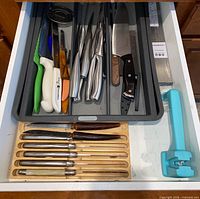 Open drawer showing knives in grey organizer, chef knife, steak knives, plastic handle knives, stainless knives, blue handheld sharpener