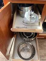 Cabinet shelf with KitchenAid hand mixer, beaters, stacked stainless bowls and nested colanders