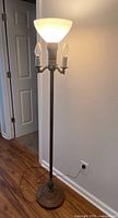 Full view of brass torchiere floor lamp plugged in and lit