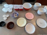 Full lot overview on countertop showing all cups, Pyrex dishes with lids, large red bowl, decorative bowls, cereal bowls and condiment dishes