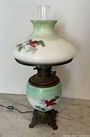 Full view of hurricane lamp showing glass shade, base, chimney, cord, cast iron stand