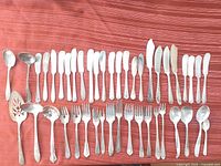 Full layout of all silverplate knives, forks, spoons and server on red cloth