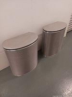 Two identical silver mesh hampers side by side against wall