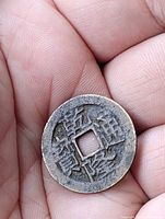 Obverse of bronze cash coin held in hand, showing Chinese characters and square hole
