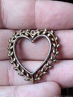 Front view of gold-tone open heart pendant on hand for scale