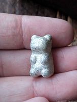 Front view of pewter teddy bear ingot on fingertips for scale