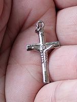 Front view of silver-plated crucifix pendant in hand