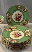 Stack of twelve green-rimmed floral plates showing pattern and gilt trim