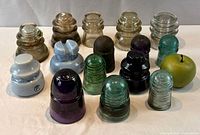 Front view of all 15 insulators showing variety of colours and shapes with size-reference apple