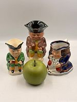 Front view of three Toby jugs with size reference apple