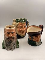 Three ceramic Toby jugs standing side by side showing different character faces and sizes