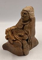 Front view of stone sculpture showing seated Indigenous figure, facial details, and object held