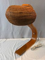 Front view of lamp showing rattan shade and curved wood base with cord
