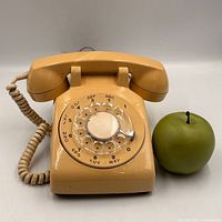 Front view of beige Northern Telecom rotary dial telephone beside reference apple