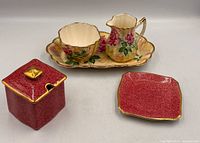 All five pieces group view: red lidded box, red tray, floral tray, sugar bowl, creamer