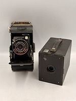 Front view of Ensign Singlo folding camera and Kodak box camera showing lens, bellows, and exterior condition