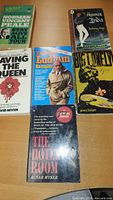 First image shows six paperback books including Prisoner of Zenda, Saving the Queen, Robert Ludlum Sampler, Big Lonely, The Hotel Room and a green Norman Prince/Stay Alive title