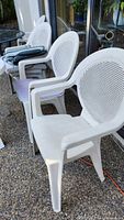 Three white resin patio chairs with cushions visible