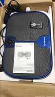 Top view of vibration plate inside box with manual and remote visible