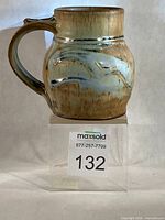 Full view of mug front on acrylic stand showing handle, glaze colors and lot number