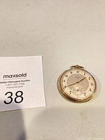 Front view of Elgin gold-tone pocket watch next to lot number