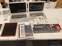 Overview of lot showing two MacBooks, iPad, tablet case, vehicle mount box, cables, scanner, remote