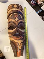 Full view of carved wood mask beside tape measure