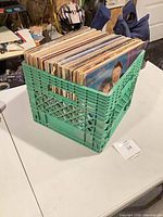 Green plastic crate filled with vinyl records on table