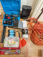 Overall view of Bosch drill kit, socket set, extension cord, power block, power strips, paracord, hammer, drop cloth, fastener box, ruler